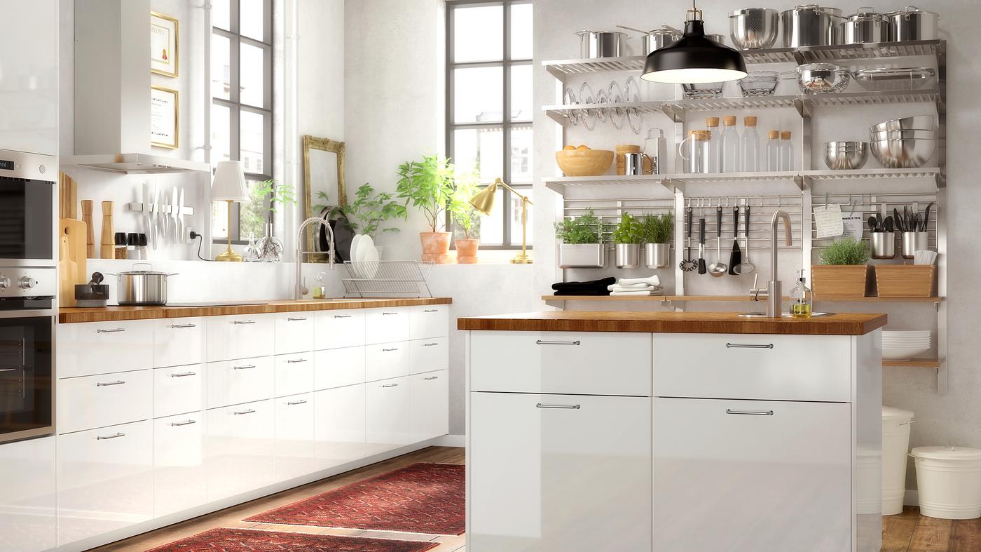 A large white kitchen with an island and white high gloss doors, an oak worktop and an open shelving unit on a wall.