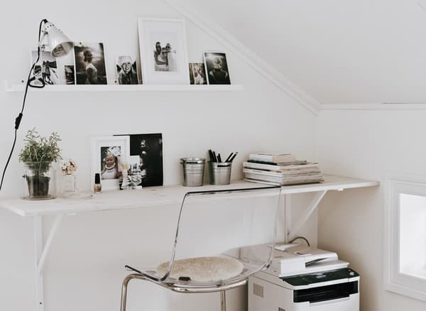 A large white shelf mounted to the wall and used as a home office desk worktop against a slanted wall to maximize space.