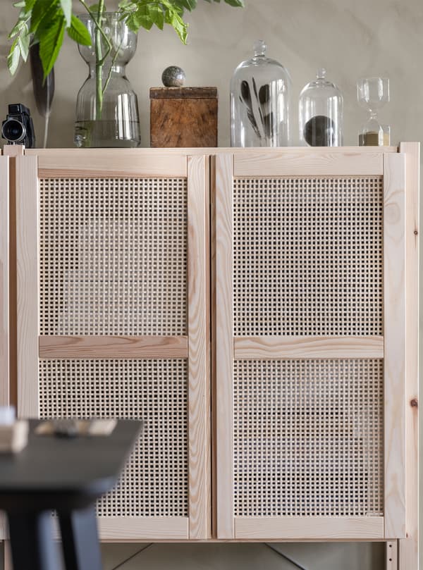 A lattice-front wall cupboard with glass vases on top with plant, feathers and other accessories in them.