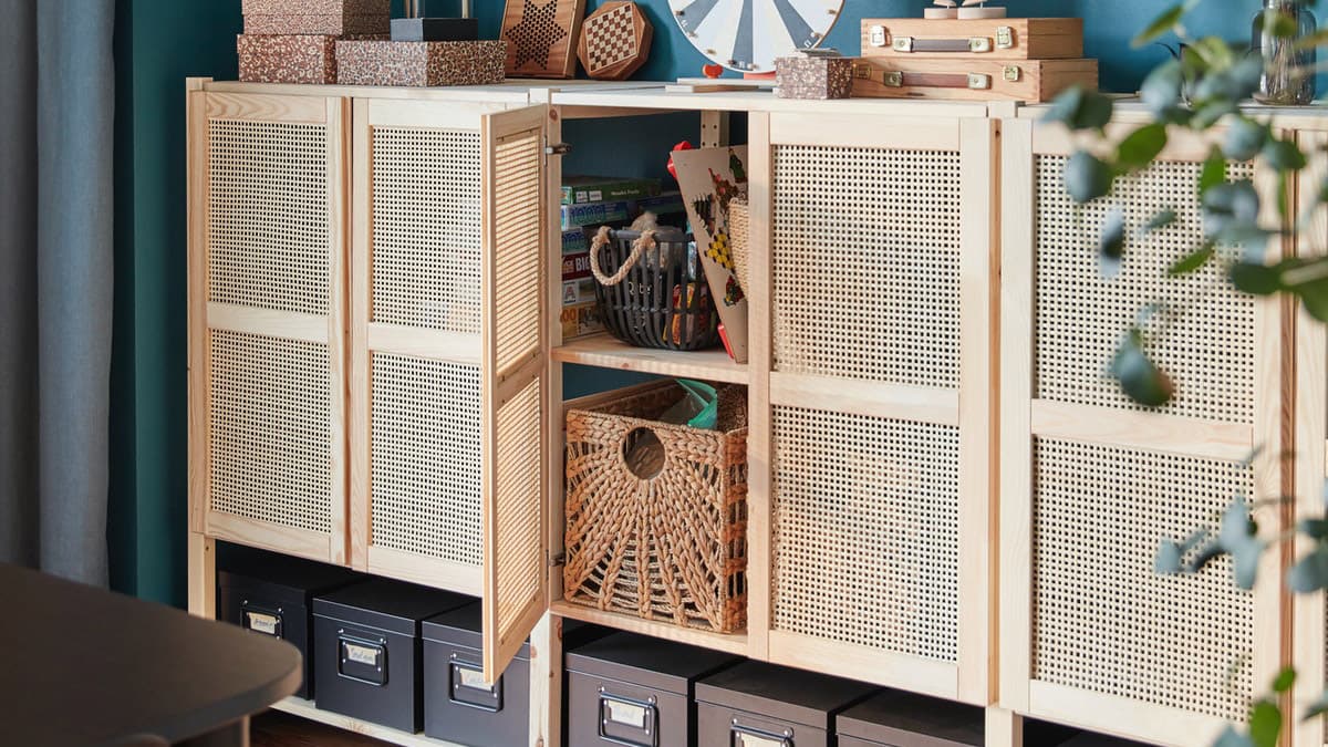 A lattice-fronted wall storage unit with one door open and storage boxes inside, plus storage boxes and accessories on top.