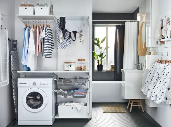 A laundry area in a bathroom with deep mesh shelves, hanging rails for drying laundry and KUGGIS plastic boxes.
