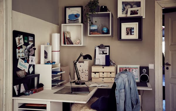 A letter tray and boxes on a corner desk with cubed EKET storage units on the wall above.