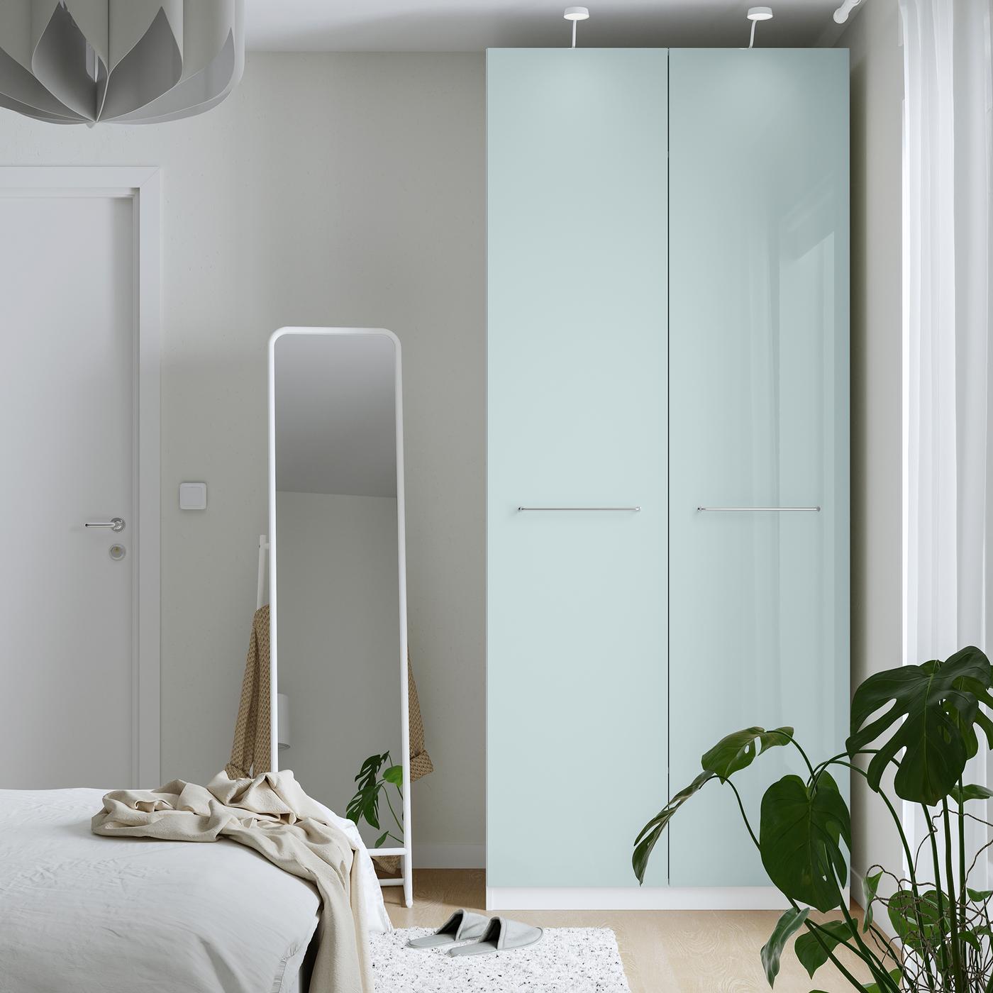 A light-blue PAX wardrobe in a bedroom with a freestanding floor mirror to the left of it
