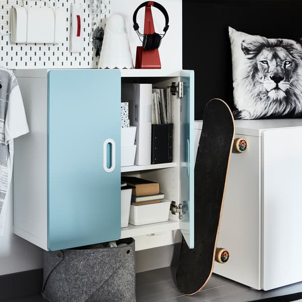 A light blue wall cabinet with organisers inside, a white lamp and a lion-patterned cushion cover.