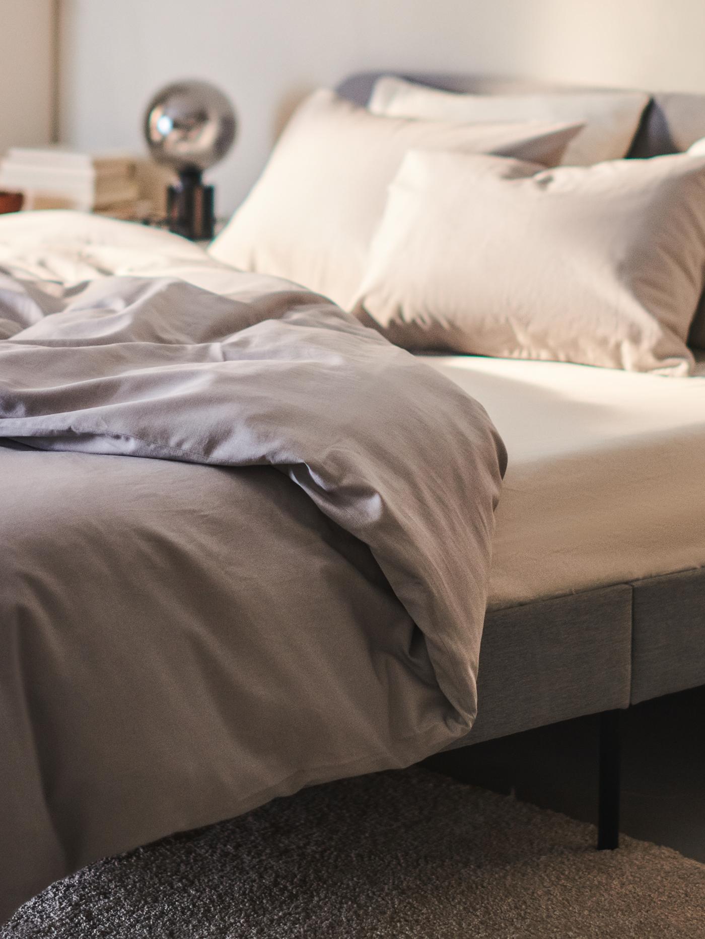A light grey SLATTUM upholstered bed frame with an ÅKREHAMN foam mattress and NATTSVÄRMARE bed linen stands against a wall.
