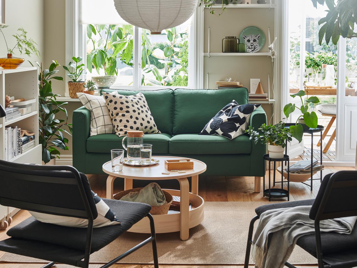 A light living room dominated by a dark-green PÄRUP loveseat sofa, graphic-pattern textiles, wood accents and leafy plants.