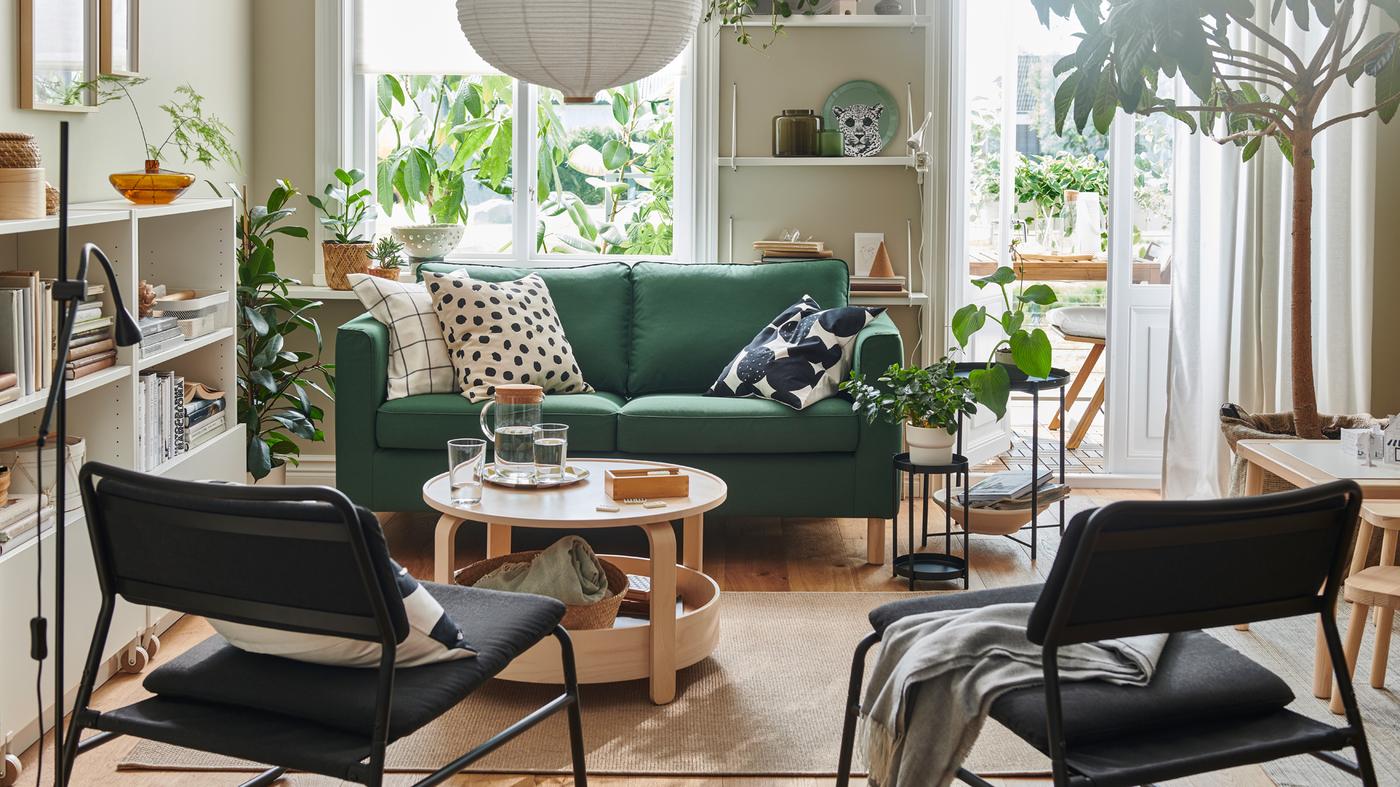 A light living room dominated by a dark-green PÄRUP two-seat sofa, graphic-pattern textiles, wood accents and leafy plants.