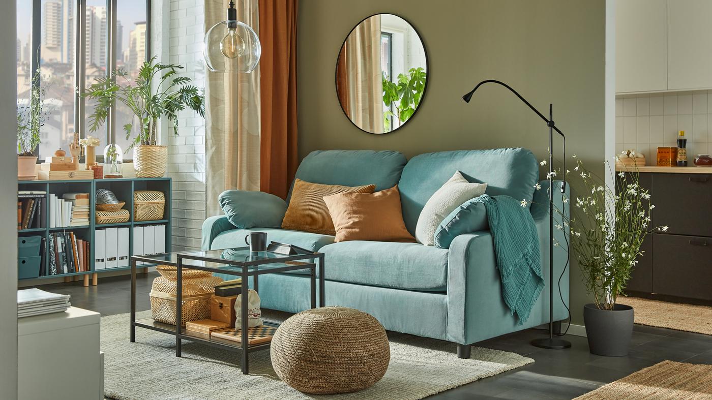 A light turquoise sofa with high back, nesting tables, grey-turquoise open cabinets by the window with books, baskets and files.