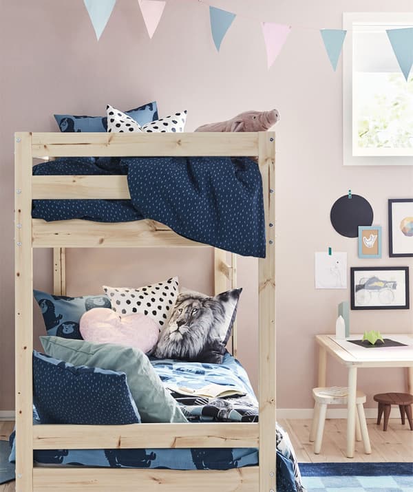 A light wood bunk bed in a child’s bedroom with blue bedding and pink walls.