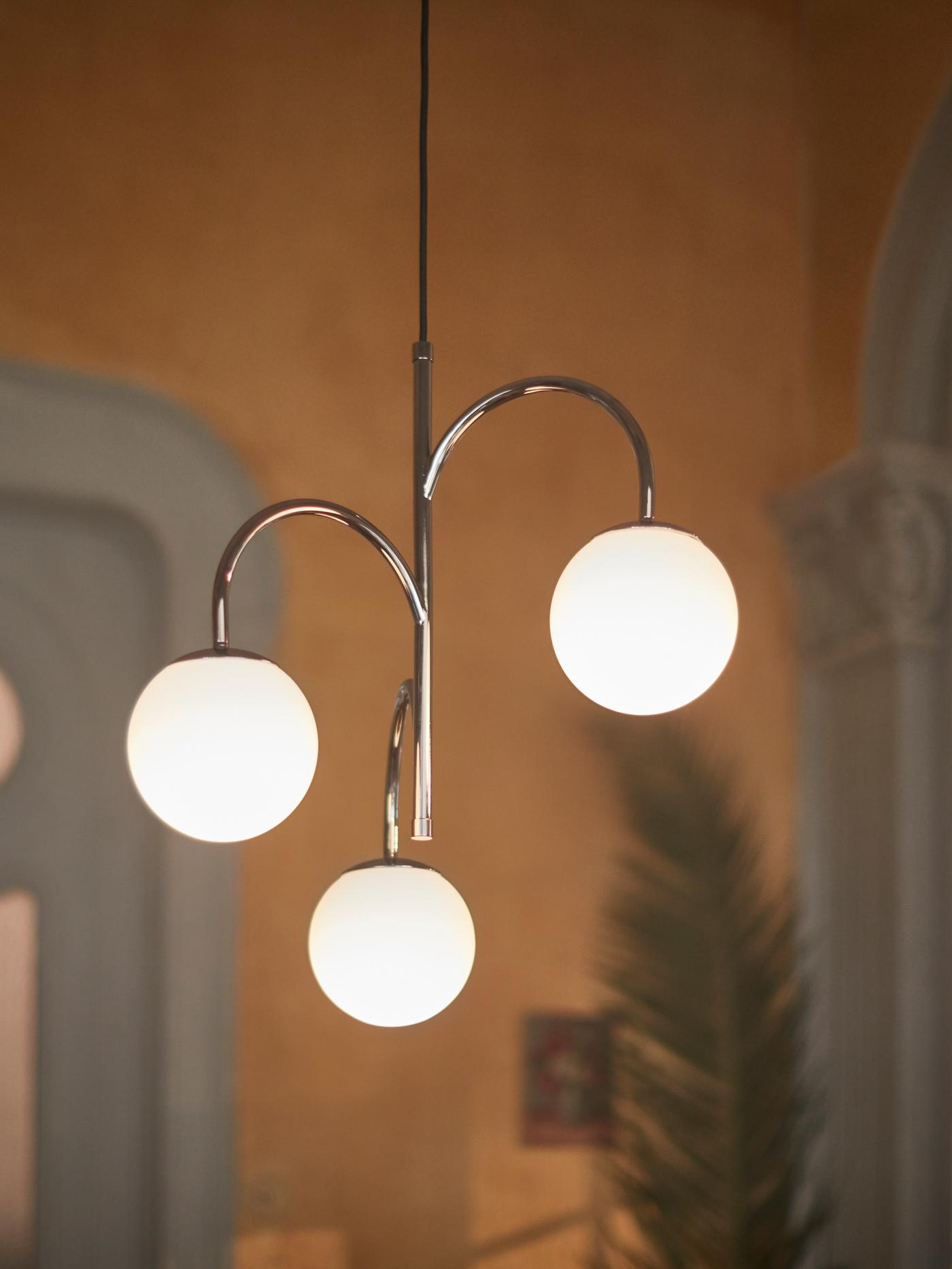 A lighting unit with three lamps in it, hanging from a ceiling in a living room setting with a green plant.