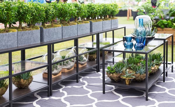 A line of tables with potted plants on top and below.