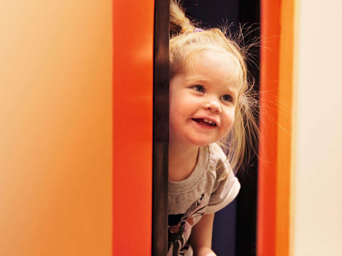 A little girl looking out from a wall, laughing.