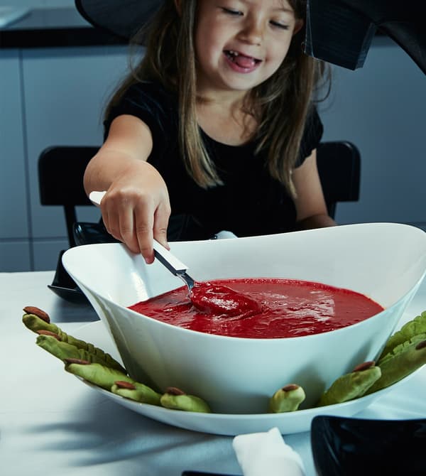 A little girls scoops some red soup.