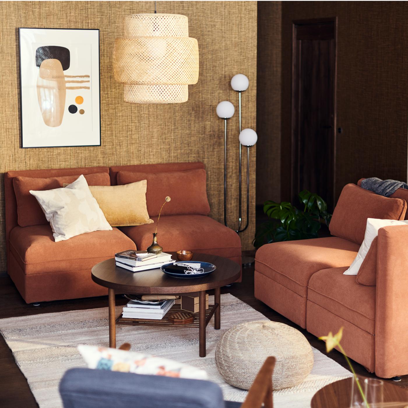 A living area with VALLENTUNA modular sofas in rust below a bamboo SINNERLIG pendant lamp.