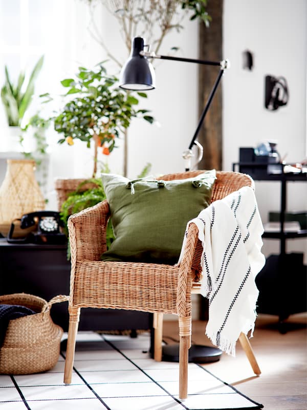 A living room area in black, white and green with large plants, an AGEN rattan chair and accents in natural materials.