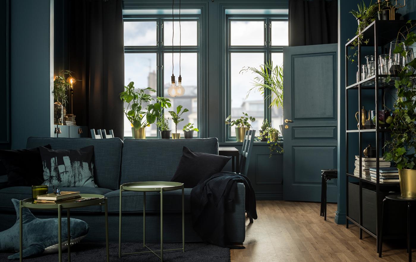 A living room styled in a colour palette of deep greens, gold and black, and decorated with a soaf and dining area.