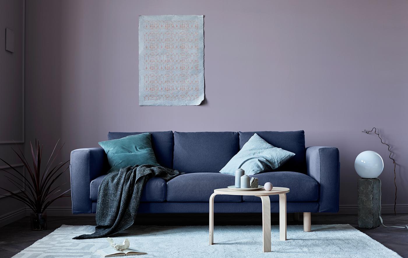 A living room updated for autumn has a grey sofa, pink walls, blankets, and natural elements like stone.