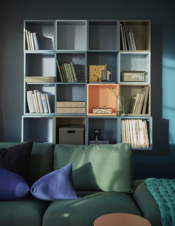 A living room wall covered in EKET cabinets, mounted together in rows to make a unified square to hold books and mementos.