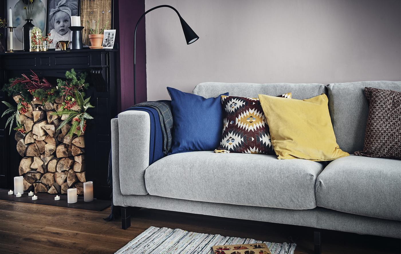 A living room with a grey sofa, lighting and a log-filled fireplace.