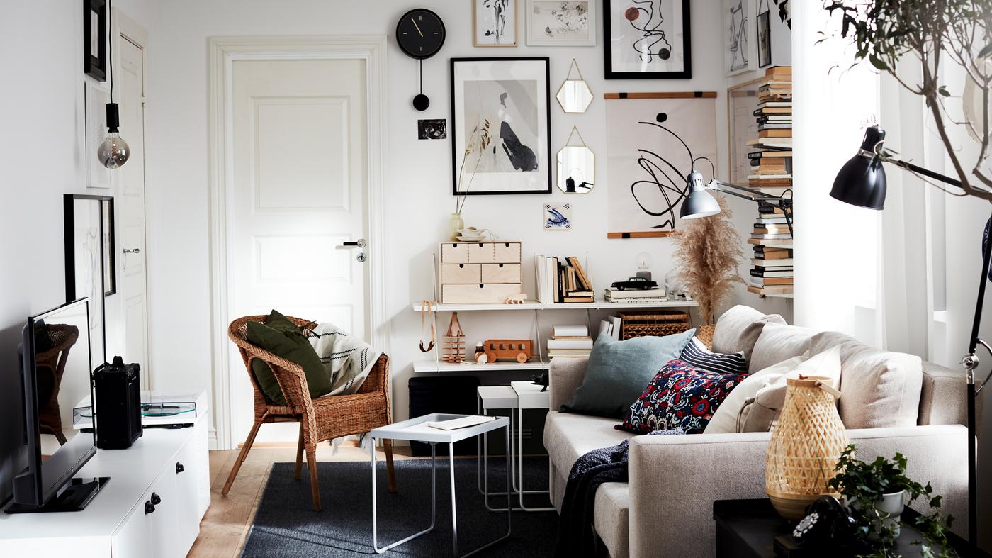 A living room with a sofa-bed, a rattan/bamboo chair, a TV bench, a dark grey rug, a black wall clock and black lamps.