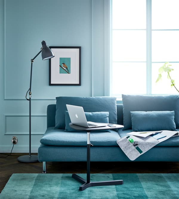A living room with a sofa, floor lamp, hanging wall organiser and adjustable laptop stand for an efficient couch desk.