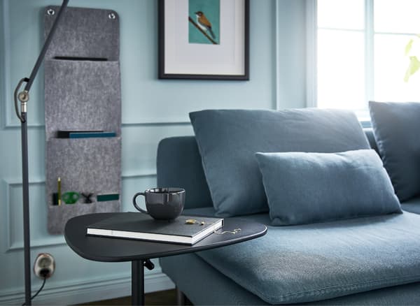 A living room with a sofa, floor lamp, hanging wall organiser and adjustable laptop stand for an efficient sofa desk.