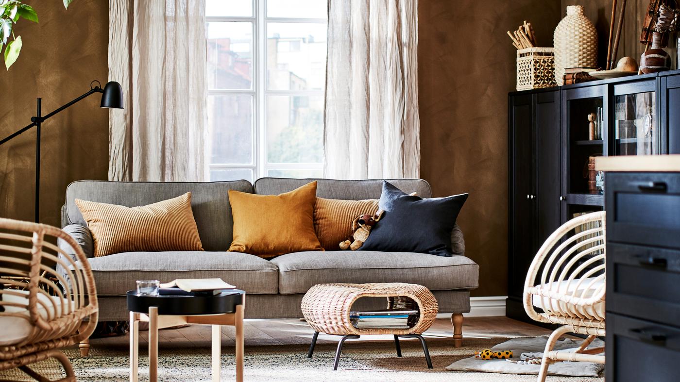 A living room with a sofa, two jute rugs, two rattan armchairs, beige linen curtains and cabinets.
