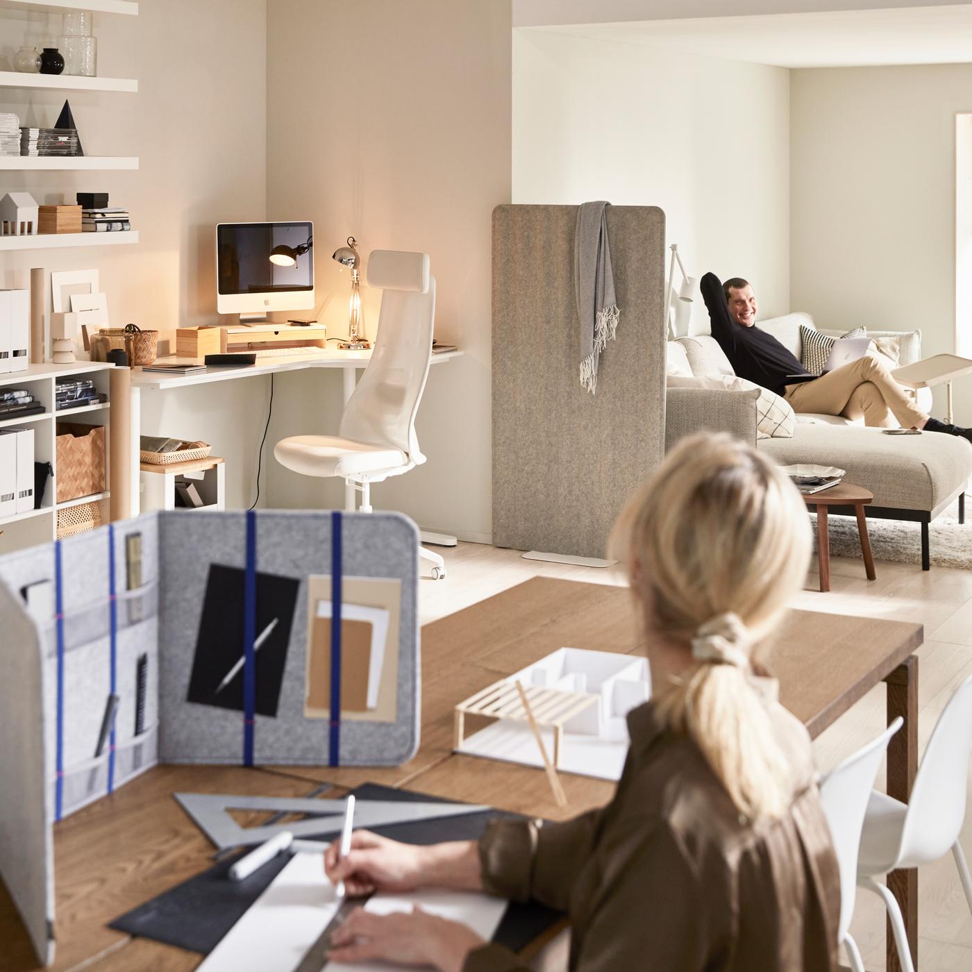 A living room with a woman using ÖVNING desk divider to study, a corner office with BEKANT desk, and a man is sat on a sofa.