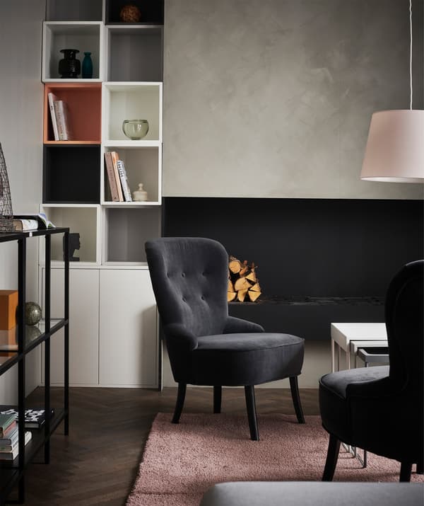 A living room with black armchairs and a pink rug, surrounded by display storage on and against the walls.