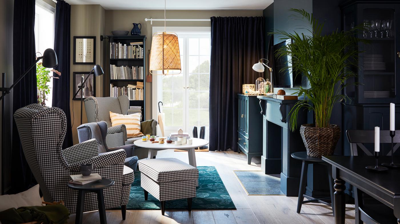 A living room with two houndstooth-patterned wing chairs, a green rug, a pendant lamp in bamboo and a round coffee table.