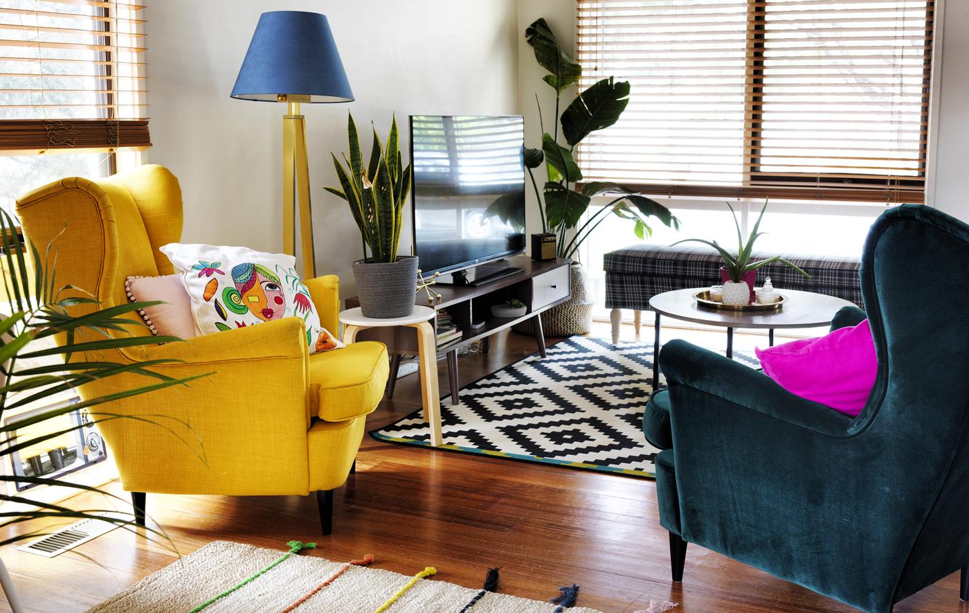 A living room with two winged armchairs in yellow and dark green, a black and white rug and TV unit.