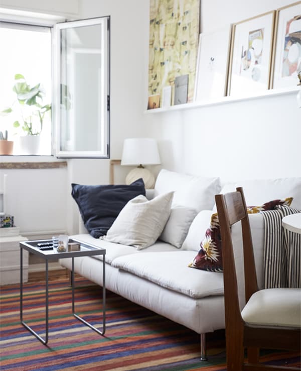 A living room with white walls, white sofa and colourful patterned rug.