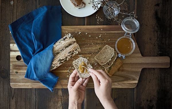 A loaf of seeded bread and jar of honey on a wooden board.