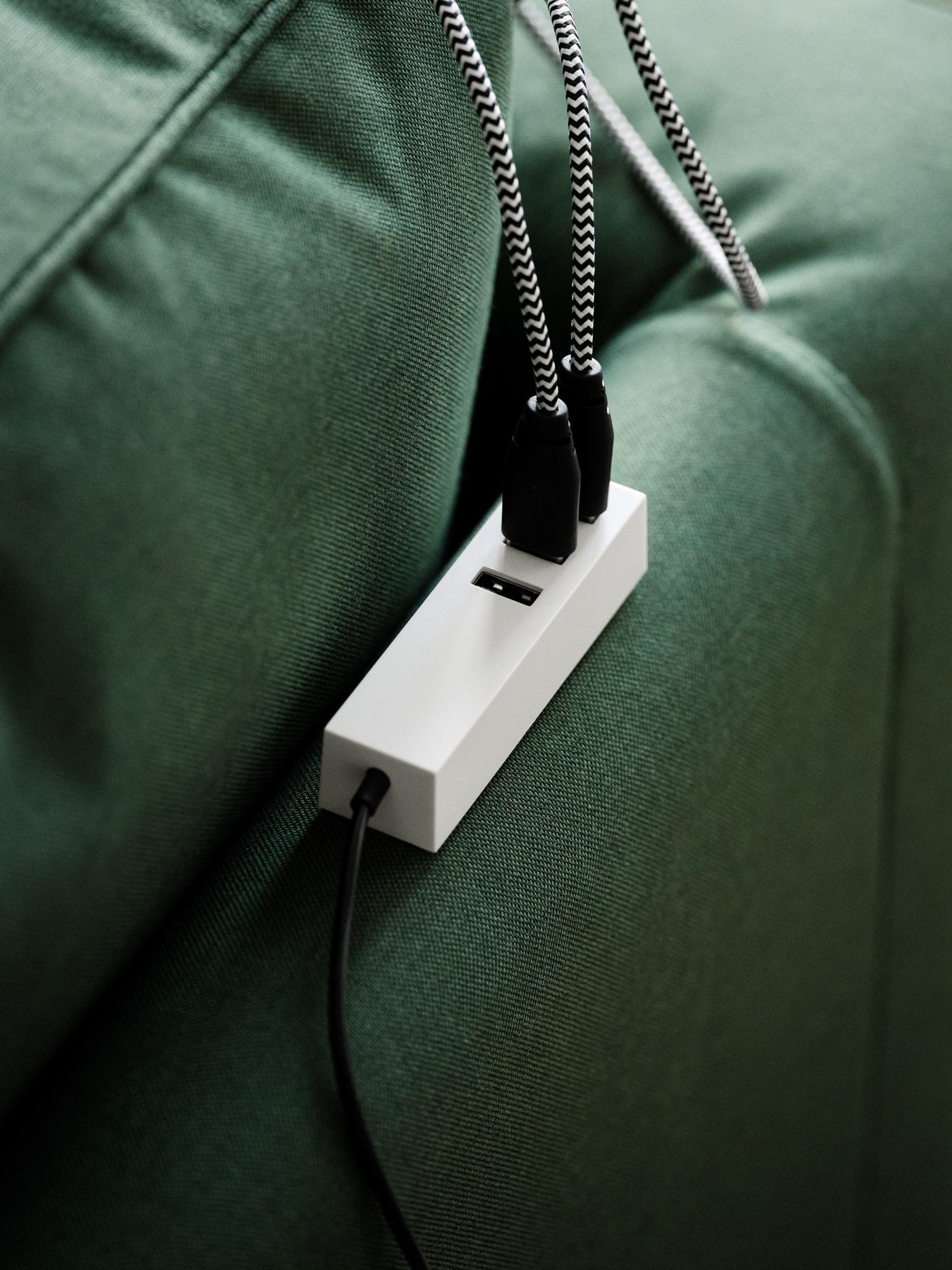 A LÖRBY magnetic USB charger placed on the back of a green PÄRUP sofa with two cables connected to it.