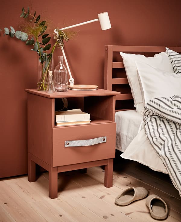A made-over bedside table with a lamp and some vases on it stands next to a bed.