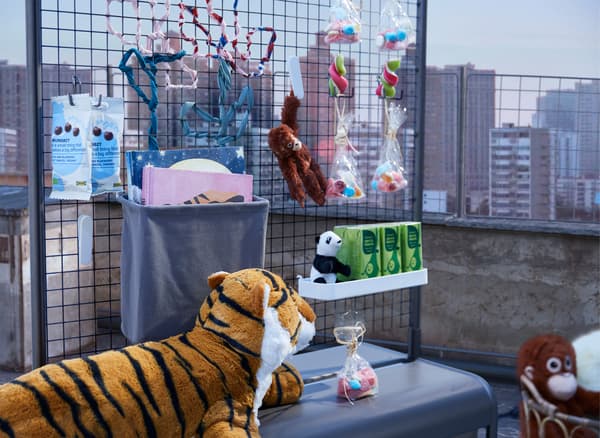 A makeshift refreshment stand with snacks and drinks, placed on a daytime rooftop and guarded by a fierce tiger.