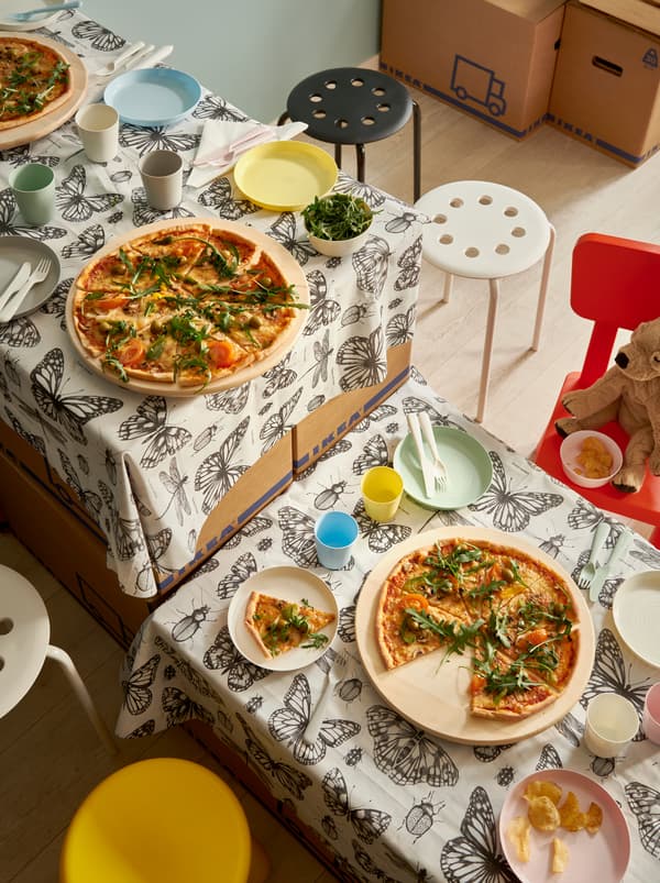 A makeshift table made of moving boxes and SOMMARMALVA shower curtain as tablecloth, set with pizzas on SNUDDA lazy Susans.