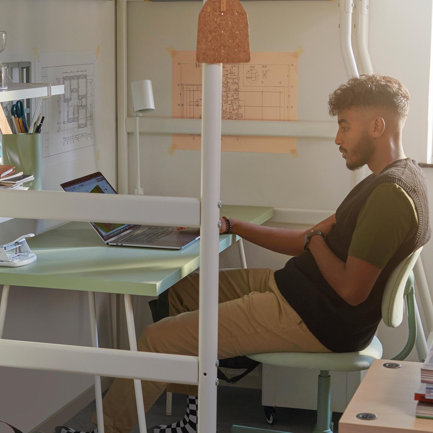 A male student sits on a BLECKBERGET swivel chair at a LAGKAPTEN/TILLSLAG desk, which is underneath a VITVAL loft bed.