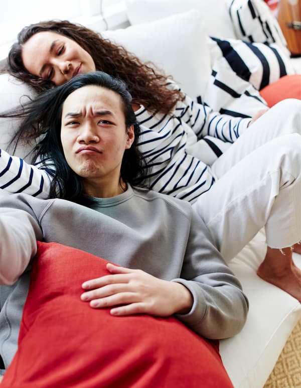 A man and a woman nestled together on a white sofa, surrounded by black-and-white striped and coloured cushions.