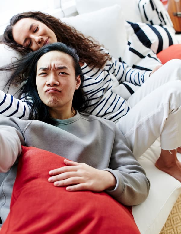 A man and a woman nestled together on a white sofa, surrounded by black-and-white striped and coloured cushions.