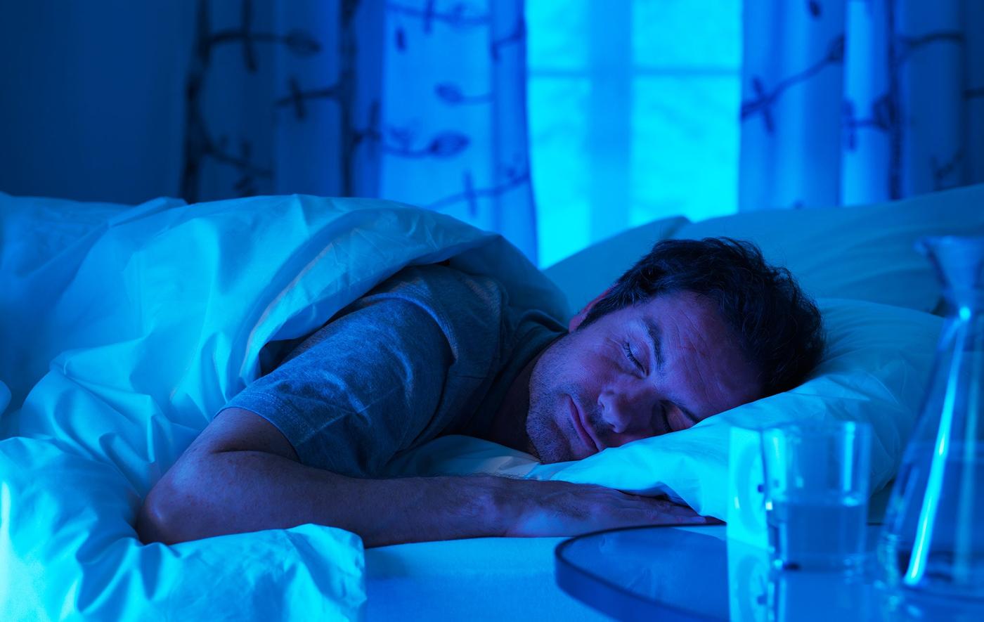 A man asleep on his side in a bedroom with dimmed light.