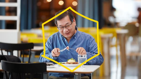 A man eating meatballs in an IKEA restaurant. A yellow frame in the shape of a hexagon on top of the image.