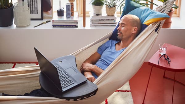 A man is resting in a hammock with a laptop on his lap.