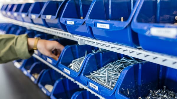 A man is taking screws out of a blue container to use them as spare parts.