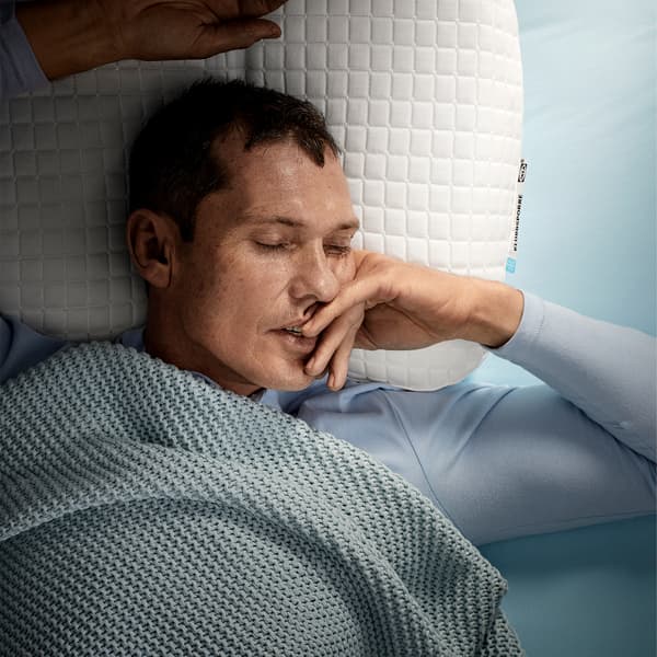 A man, laying on his back, is sleeping deeply on IKEA KLUBBSPORRE ergonomic pillow.