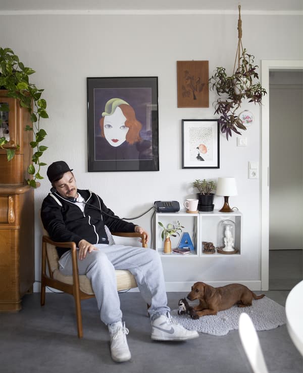 A man on the phone, sitting in a chair, with a dog on the floor by his feet.