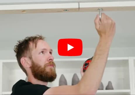 A man screws a board into the ceiling, a red Youtube play button sits overlay.