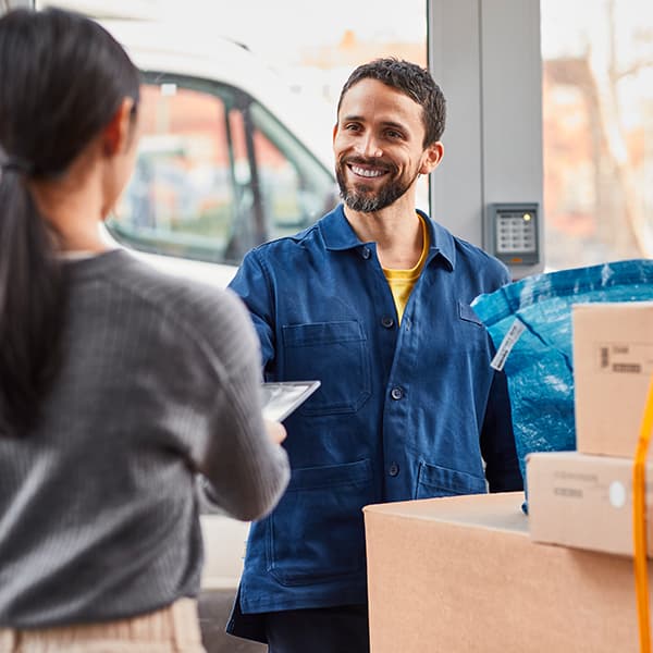 A man stands in front of a woman with IKEA boxes and a blue FRAKTA bag. He is delivering furniture and accessories to her business.