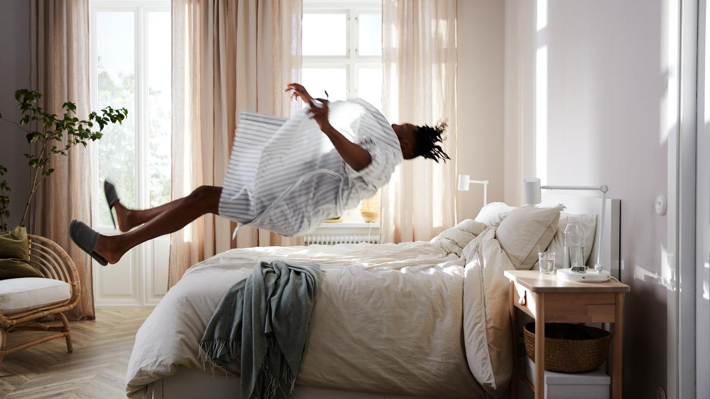 A man throws himself backwards to land on top of a MALM bed with a VATNESTRÖM pocket sprung mattress and white bed linen.