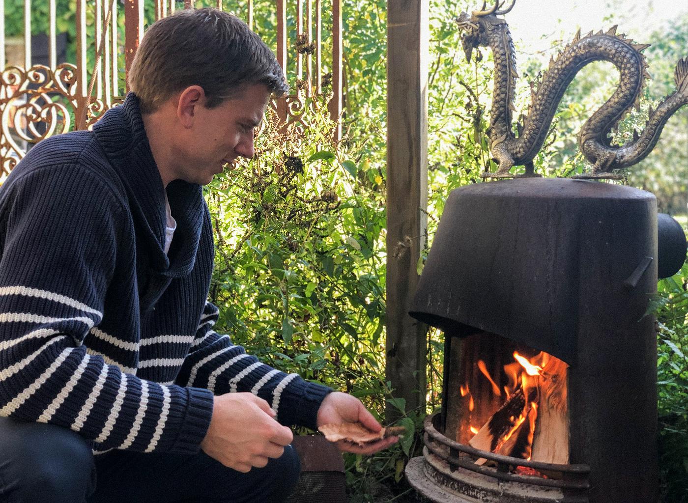 A man wearing a navy blue sweater with white stripes is busy making a fire in a fireplace.